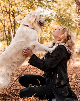 Pet care. Blond caucasian woman playing with her golden retriever in autumn park