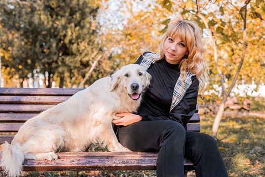 Pet care concept. Young blond woman with her retriever dog on the bencj in the park