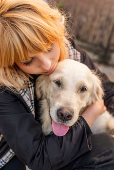 Pet care concept. Blond caucasian woman hugging her golden retriever dog outdoors