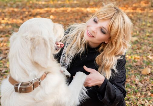 Pet care concept. Blond caucasian woman playing with her golden retriever in autumn park