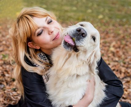 Pet care concept. Blond caucasian woman hugging her golden retriever dog outdoors