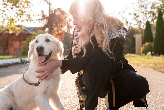 Pet care concept. Blond caucasian woman hugging her golden retriever dog outdoors in the sunset