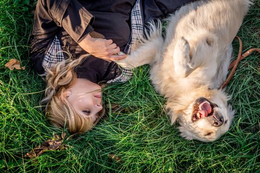 Pet care concept. Beautiful caucasian woman laying on the grass with her golden labrador retriever dog at a park in the sunset