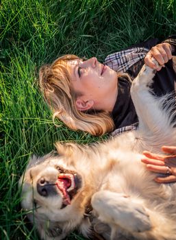 Pet care concept. Beautiful caucasian woman laying on the grass with her golden labrador retriever dog at a park in the sunset