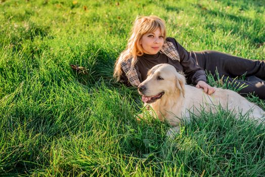 Pet care concept. Beautiful caucasian woman laying on the grass with her golden labrador retriever dog at a park in the sunset