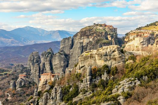 Four monasteries of Meteors: Roussanou, Monastery of Agios Nikolaos Anapafsas, Varlaam and Grand Meteora scattered on the steep cliffs with mountains panorama in background, Kalampaka, Trikala, Thessaly, Greece