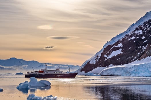 Touristic antarctic cruise vessel among the icebergs with glacier in background, Neco bay, Antarctica