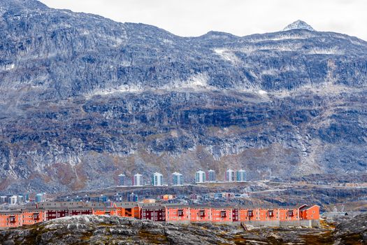 Rows of colorful modern Inuit houses among mossy stones with grey steep slopes of Little Malene mountain in the background, Nuuk, Greenland