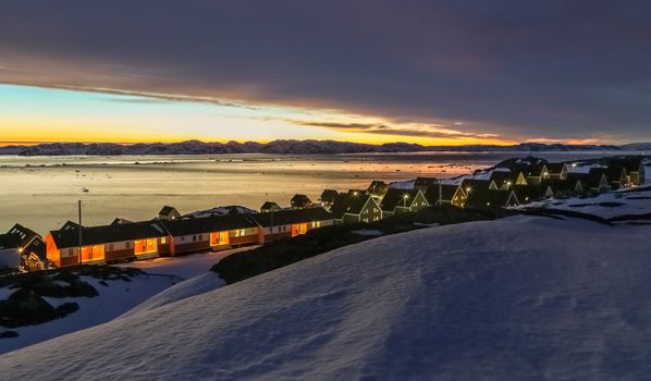 Frozen inuit houses among rocks and snow at the sunset fjord in outskirts of arctic capital Nuuk, Greenland