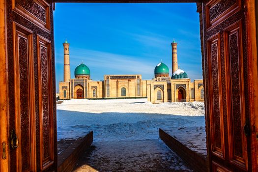 Winter shot of blue domes, mosques and minarets of Hazrati Imam medrese with wooden ornated doors in the foreground, religious center of Tashkent, Uzbekistan