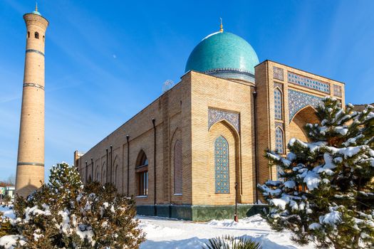 Snow and trees around ornated mosque and minaret of Hazrati Imam complex, religious center of Tashkent, Uzbekistan