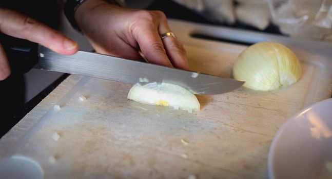 woman cuts onions on a white plastic board in a kitchen