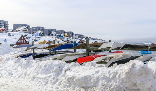 Inuit kayaks stored for a winter time in snow with Modern buildings and small cottages in the background, Nuuk old city harbor, Greenland8