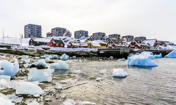 Modern buildings and small cottages with icebergs drifting in the lagoon, Nuuk old city harbor, Greenland