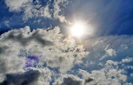 Beautiful view at bright sunbeams with some lens flares and clouds in a blue sky