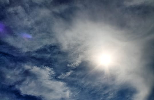 Beautiful view at bright sunbeams with some lens flares and clouds in a blue sky