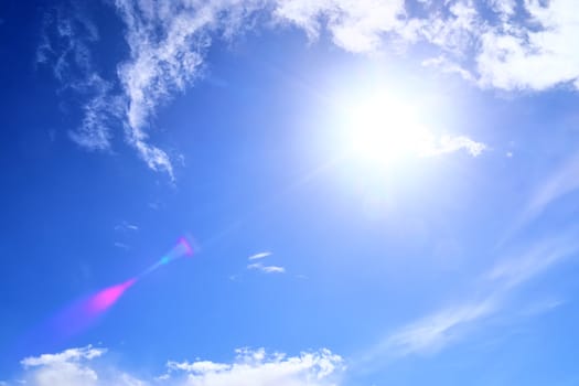 Beautiful view at bright sunbeams with some lens flares and clouds in a blue sky