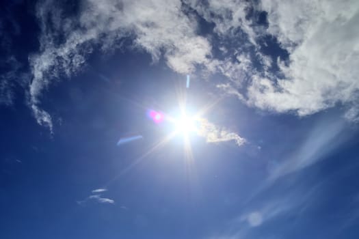 Beautiful view at bright sunbeams with some lens flares and clouds in a blue sky