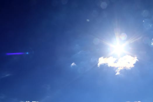 Beautiful view at bright sunbeams with some lens flares and clouds in a blue sky