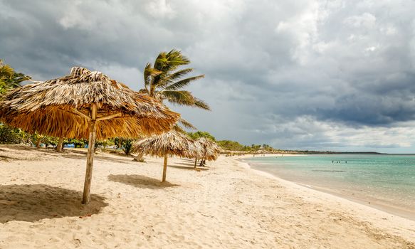 Rancho Luna sandy beach with palms and straw umbrellas on the shore, Cienfuegos, Cuba