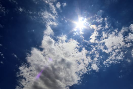 Beautiful view at bright sunbeams with some lens flares and clouds in a blue sky