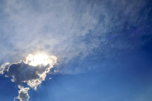 Beautiful view at bright sunbeams with some lens flares and clouds in a blue sky