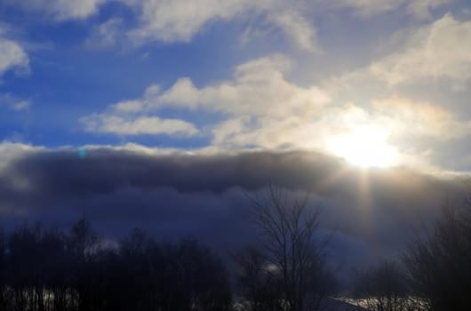 Beautiful view at bright sunbeams with some lens flares and clouds in a blue sky