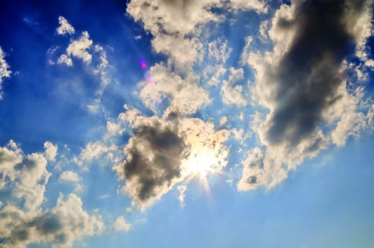 Beautiful view at bright sunbeams with some lens flares and clouds in a blue sky