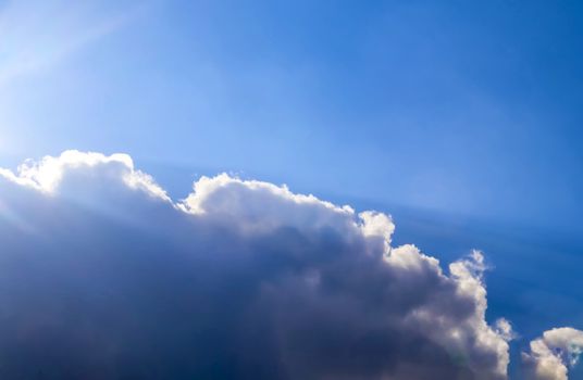 Beautiful view at bright sunbeams with some lens flares and clouds in a blue sky