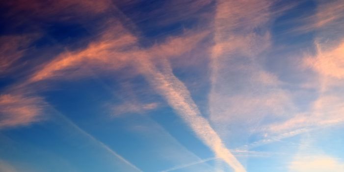 Aircraft condensation contrails in the blue sky inbetween some beautiful clouds