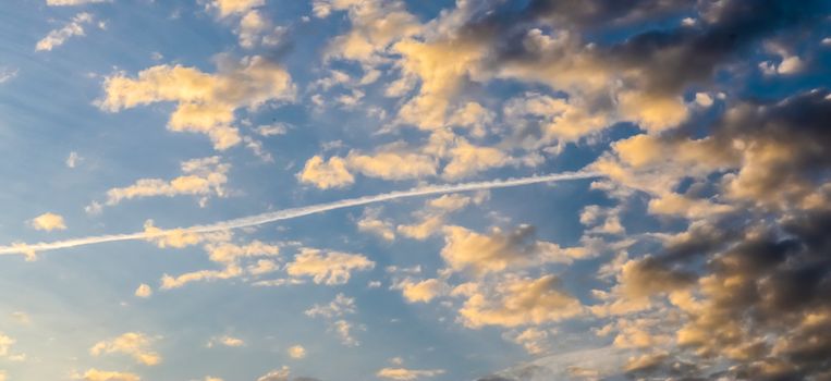 Aircraft condensation contrails in the blue sky inbetween some beautiful clouds