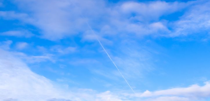 Aircraft condensation contrails in the blue sky inbetween some beautiful clouds