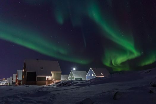 Arctic village and green waves of Northern lights over Inuit houses, in a suburb of Nuuk, Greenland