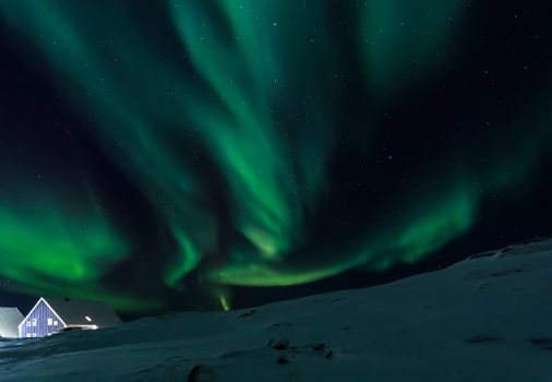Arctic village and green waves of Northern lights over Inuit houses, in a suburb of Nuuk, Greenland