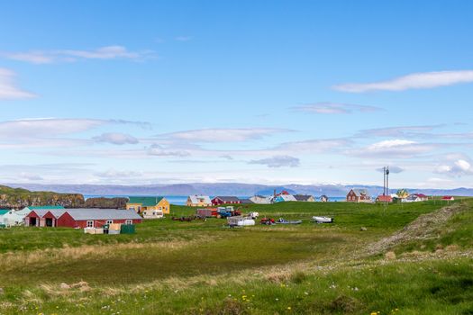 Village with living houses and meadow in foreground and sea  fjord with blue sky in the background, Flatey island, Iceland