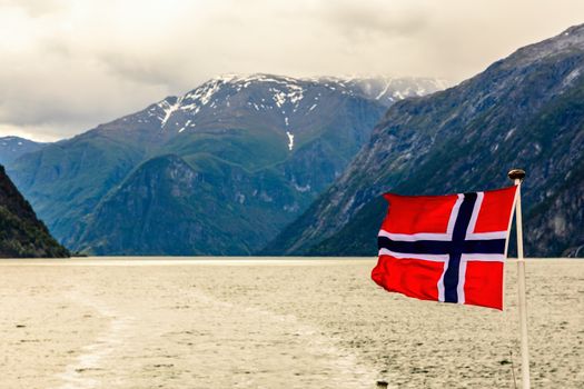 Norwegian national flag waving in the wind in Sogne fjord with mountains in the background, Aurlan, Sogn og Fjordane county, Norway