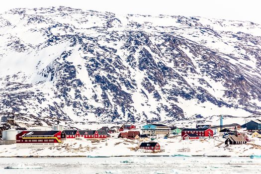 Arctic city panorama with colorful Inuit cottages and oil factory on the rocky hills covered in snow and mountain in the background, Ilulissat, Avannaata municipality, Greenland