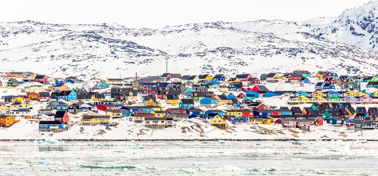 Arctic city center panorama with colorful Inuit houses on the rocky hills covered in snow with snow and mountain in the background, Ilulissat, Avannaata municipality, Greenland