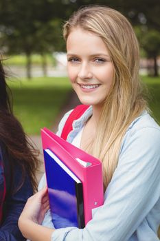 Smiling student holding binder at park