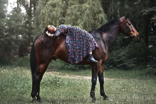 Young pretty girl laying on horseback in the forest