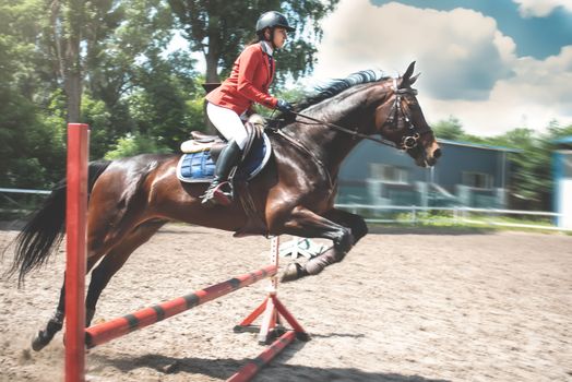 Young female jockey on horse leaping over hurdle