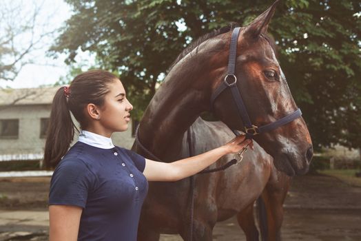 A young girl talking and takes care of her horse. She loves the animals and joyfully spends her time in their environment.