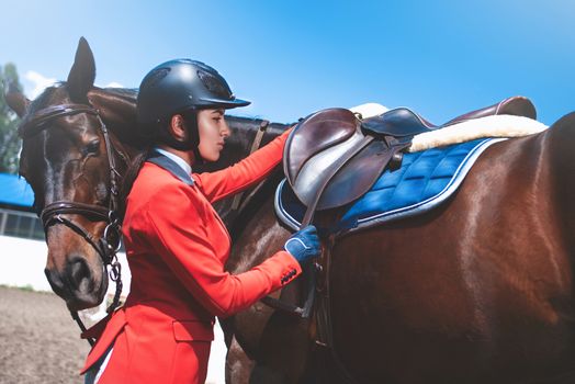 Girl jockey adjusts saddle on her horse to take part in horse races