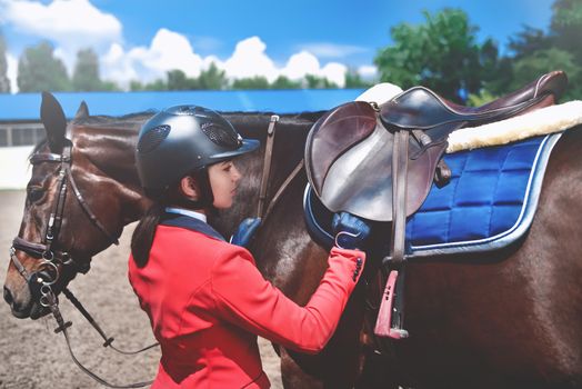 Girl jockey adjusts saddle on her horse to take part in horse races