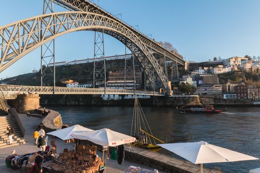 Porto, Portugal - November 30, 2018: Street atmosphere near the Dom Luiz bridge with its café terrace and its traders where people are walking on an autumn day