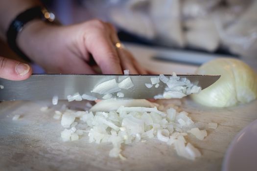 woman cuts onions on a white plastic board in a kitchen