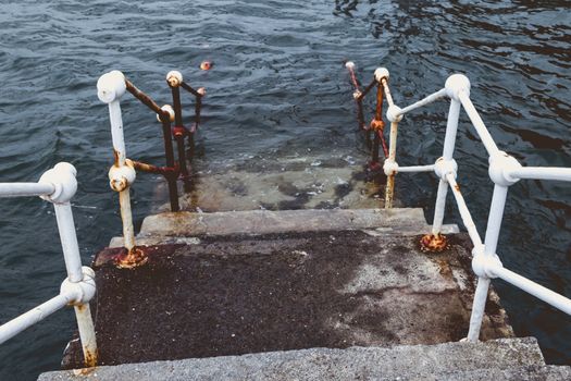 concrete staircase with white metal barriers sinking into the water - concept