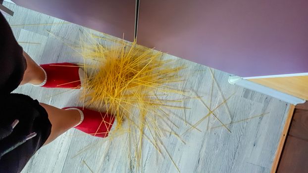 Scattered spaghetti on the floor. The woman dropped the spaghetti.