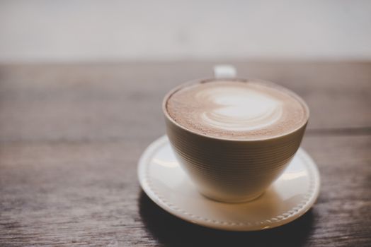 Vintage latte art coffee with heart shape on wooden table.