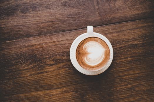 Top view of vintage latte art coffee with heart shape on wooden table.